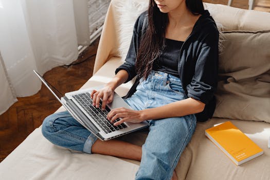 Young woman working on a laptop sitting comfortably on a sofa with natural light.