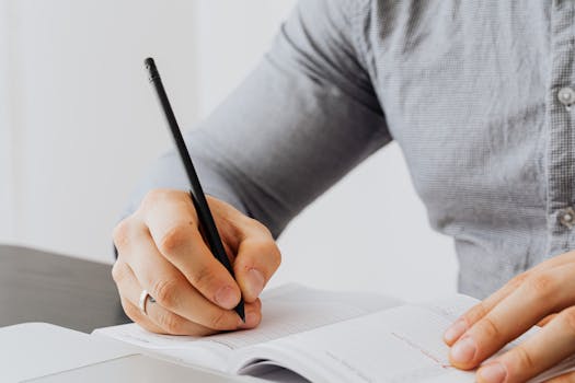 A detailed view of a person writing in a notebook with a pen, showing focus and concentration.