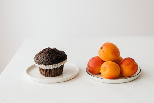 Delicious chocolate muffin paired with fresh apricots on a white surface, presenting a sweet treat.