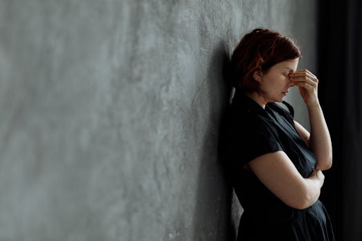 A woman in stress with eyes closed, leaning against a concrete wall indoors.