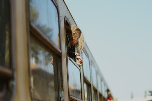 A girl leans out of a train window, traveling through Aleppo, capturing a moment of exploration and nostalgia.