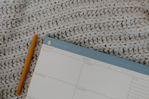 Weekly planner and pen on knitted fabric, perfect for organizing plans.