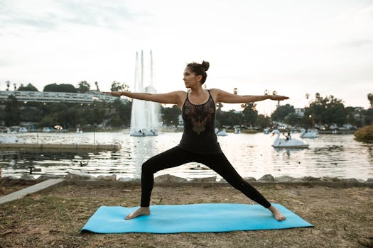 A woman in activewear performs outdoor yoga on a mat by a serene lake during sunset.