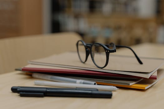 Eyeglasses resting on stacked notebooks with pens on a wooden table, perfect for education themes.
