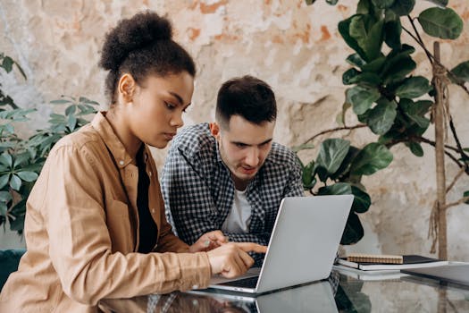 Two young adults collaborate on a project using a laptop in a modern workspace.