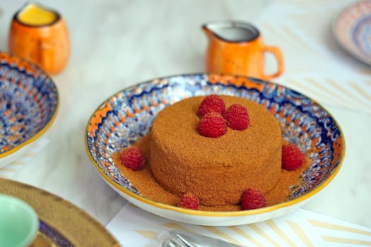 Mouthwatering honey cake topped with raspberries on an ornate plate.