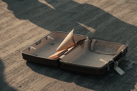 An open suitcase on a pavement with a book inside, casting shadows.