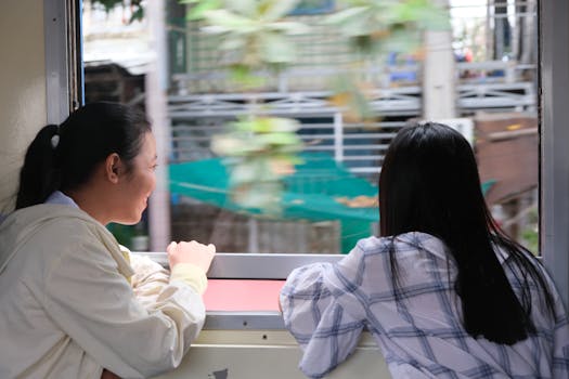 Two young women enjoying a scenic train journey in Cambodia, sharing smiles and views from the window.
