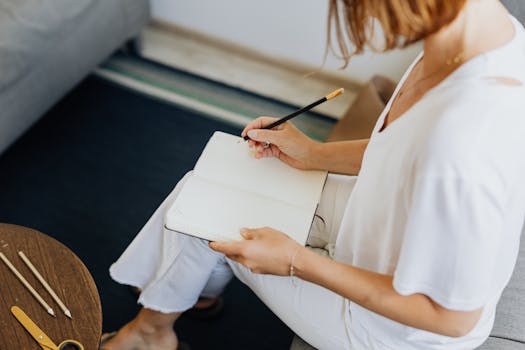 A woman in casual attire writes in a notebook on a cozy indoor sofa setting.