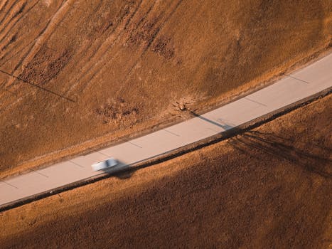 Aerial shot of a car driving on a winding road through a grassy landscape in Graz, Austria.