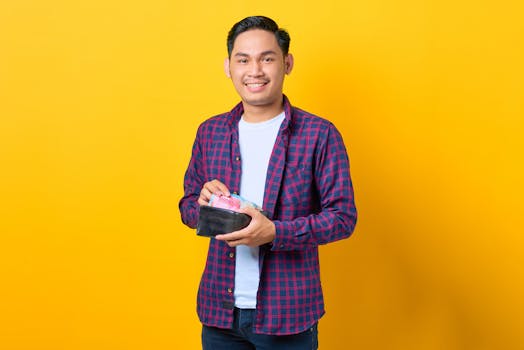 Happy young man in plaid shirt holding wallet with Indonesian rupiah against yellow background.
