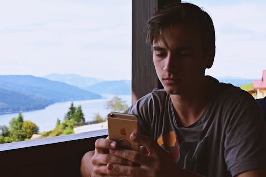 A young man using his smartphone while relaxing by a beautiful lakeside view in Bicaz, Romania.