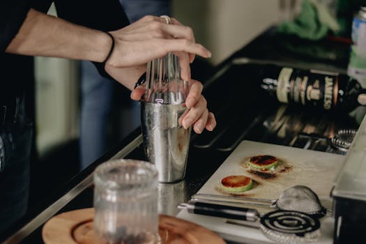 Close-up of a bartender using a shaker to mix a cocktail in a kitchen setting.