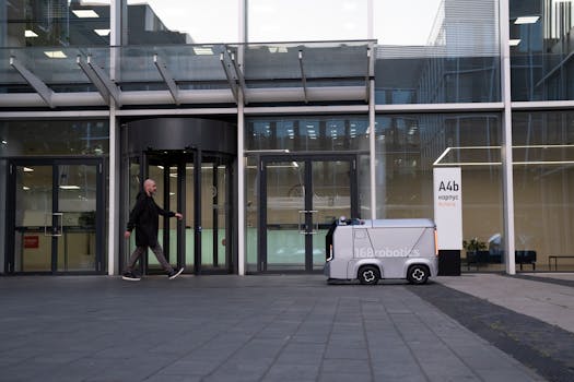 A modern office setting featuring a man and an autonomous delivery robot outside a glass-covered building.