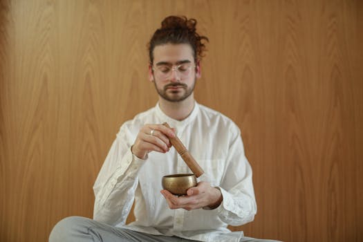 A man practicing meditation indoors with a Tibetan singing bowl, promoting relaxation and mindfulness.