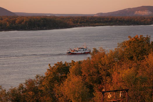 A picturesque river scene at sunset with a boat and vibrant autumn foliage.