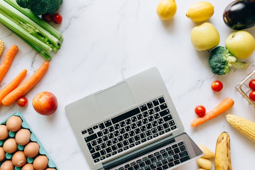 Top view of fresh veggies, fruits, and a laptop on a clean marble countertop, perfect for food blogs.