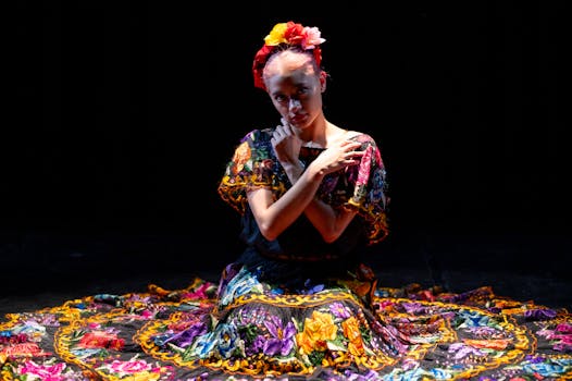 Woman in vibrant Mexican dress, kneeling with floral wreath, showcasing traditional culture.