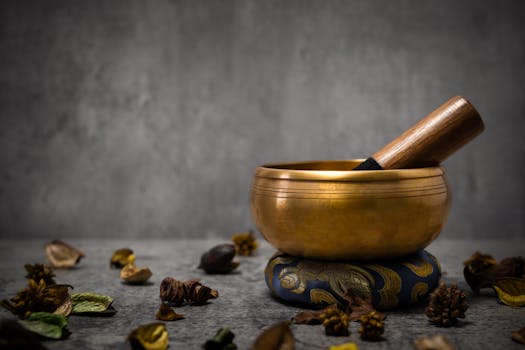 A serene scene featuring a Tibetan singing bowl with a wooden mallet, surrounded by dried plants.