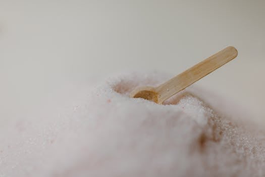A detailed view of pink Himalayan bath salt with a wooden spoon against a soft background, ideal for spa and wellness content.