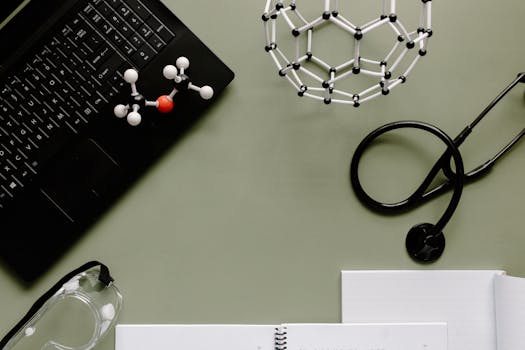 Medical workspace with laptop, molecules, and stethoscope on green background.