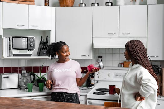Two women in a modern kitchen making smoothies, enjoying casual conversation.