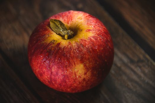 Vibrant red apple with water droplets on a rustic wooden surface, highlighting freshness.