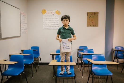 Child standing on desk in classroom holding a sign against bullying, promoting kindness and awareness.