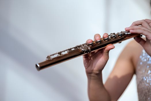 Crop unrecognizable female musician in glittering dress with bare shoulder playing flute on white background