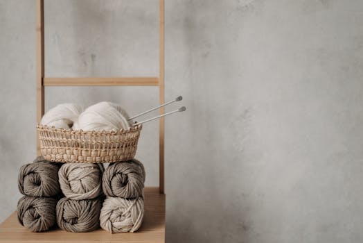 Handmade yarn and knitting needles on a wooden ladder shelf, showcasing a cozy and rustic craft vibe.