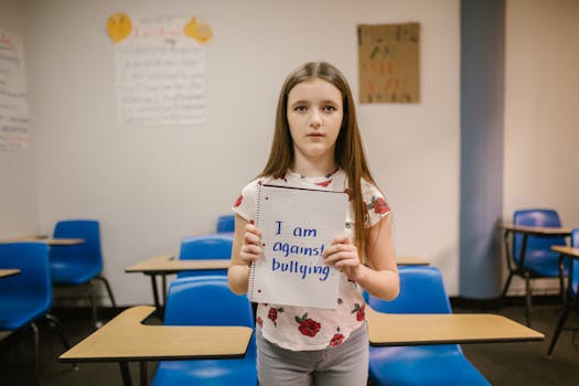 A girl stands in a classroom holding a sign against bullying, promoting awareness.