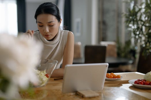 Asian woman using tablet while preparing salad in modern kitchen.