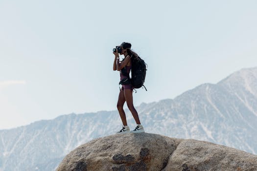 Woman photographer capturing a scenic view while hiking on a rocky mountain in summer.