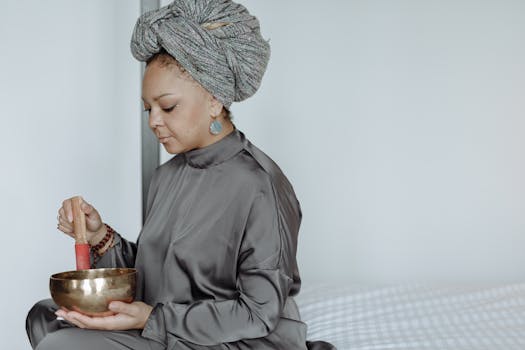 Woman in gray attire meditating indoors with a singing bowl for relaxation.