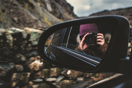 Reflective photography of a person with camera in car side mirror outdoors.